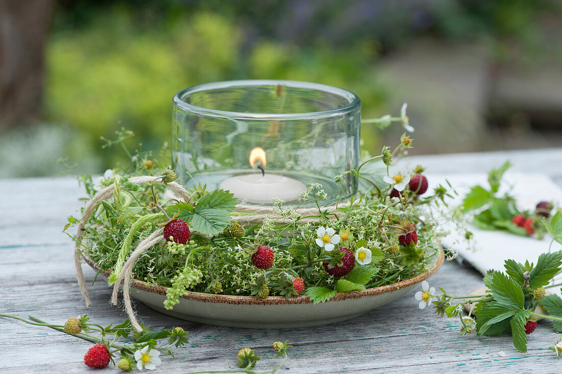 Lantern with floating candle in a wreath of wild strawberries and bedstraw