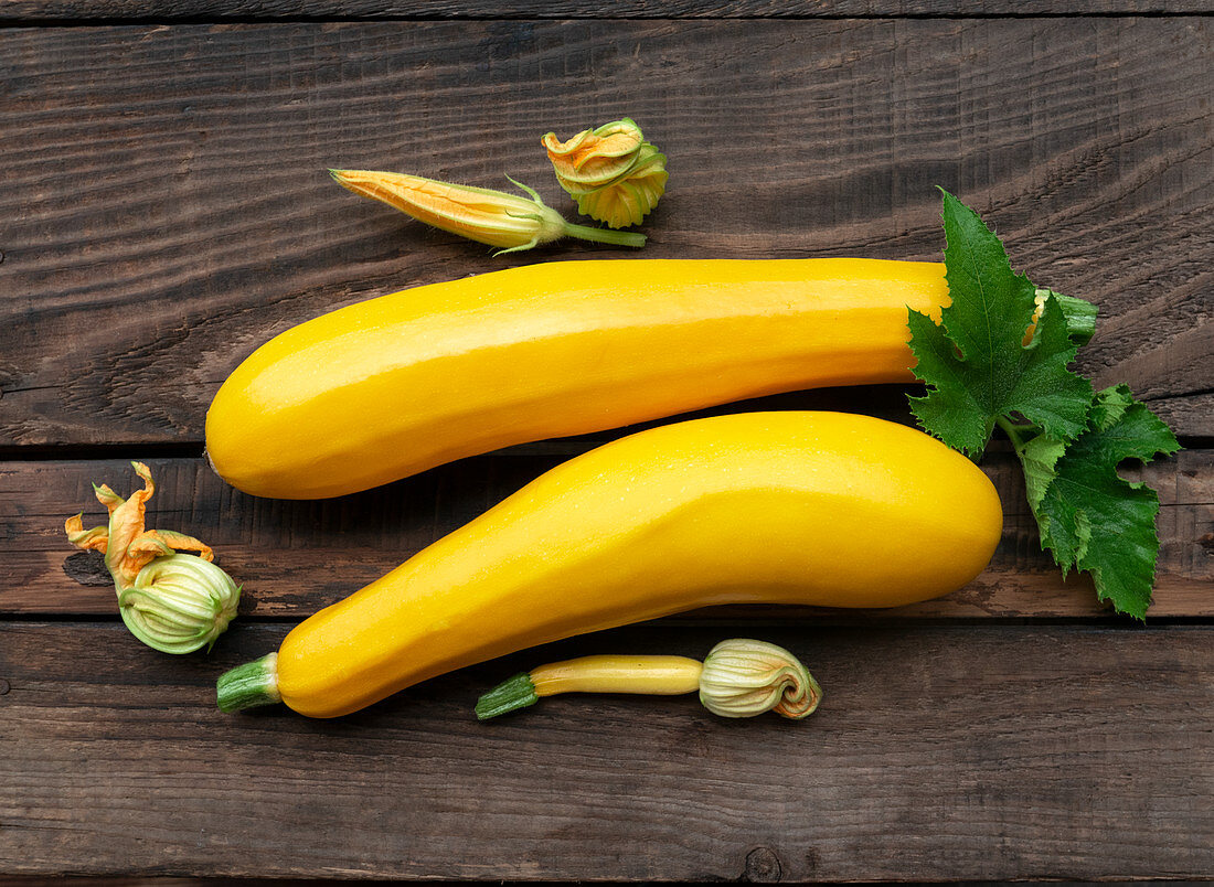 Fresh yellow zucchini and zucchini flowers on a wooden background