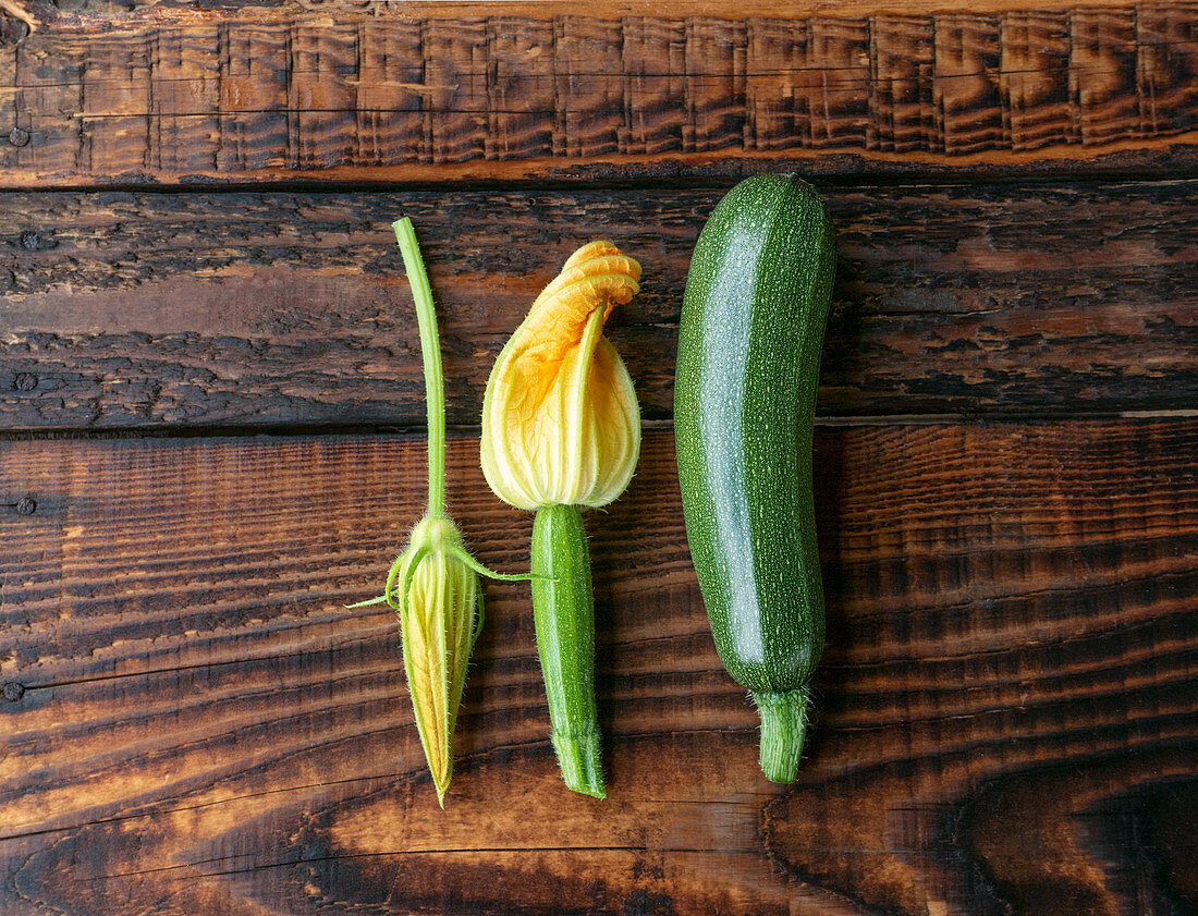 Fresh green zucchini and zucchini flowers on a wooden background