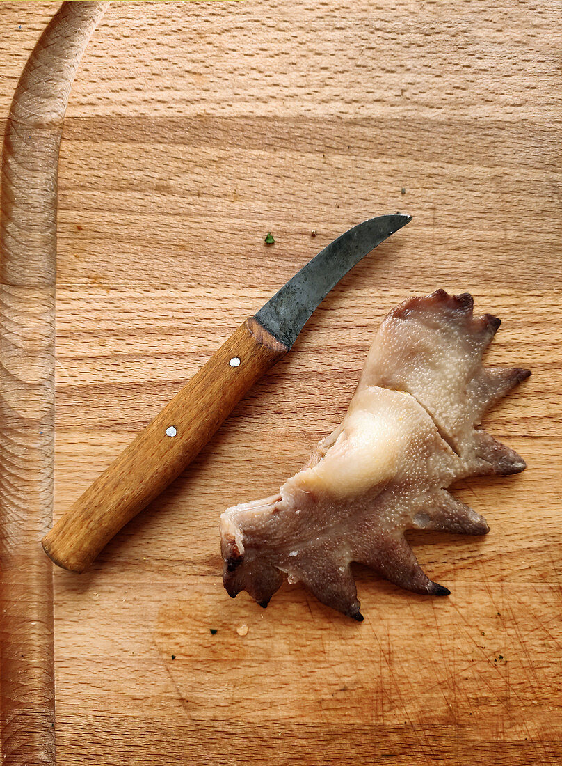 Ein roher Hahnenkamm mit Messer auf Holzuntergrund