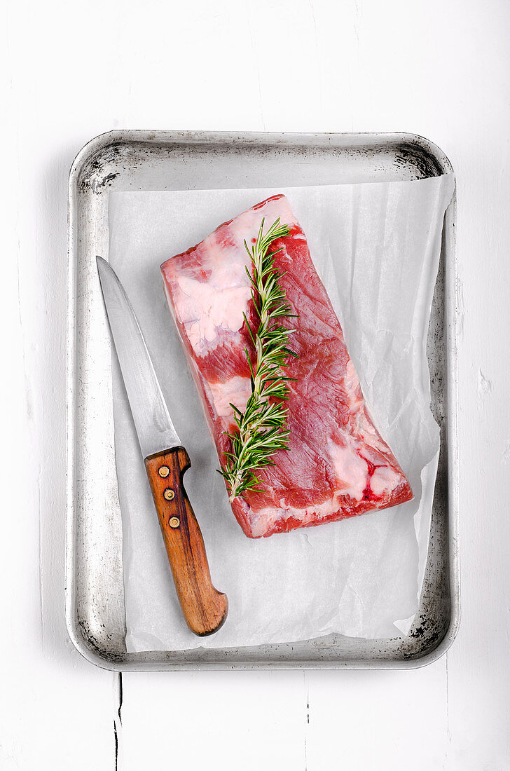 Piece of pork belly with a sprig of rosemary in an metal roasting tray