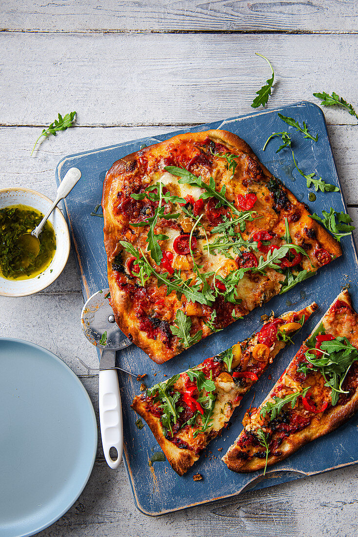 Hausgemachte Pizza mit Salami, Mozzarella, Paprika, Rucola und Basilikum-Knoblauch-Öl