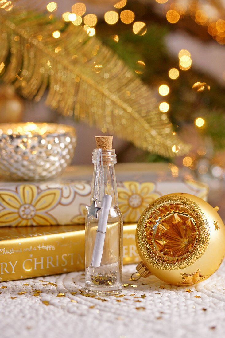 Fläschchen mit Wunschzette, umgeben von Weihnachtsdekoration in Goldfarben