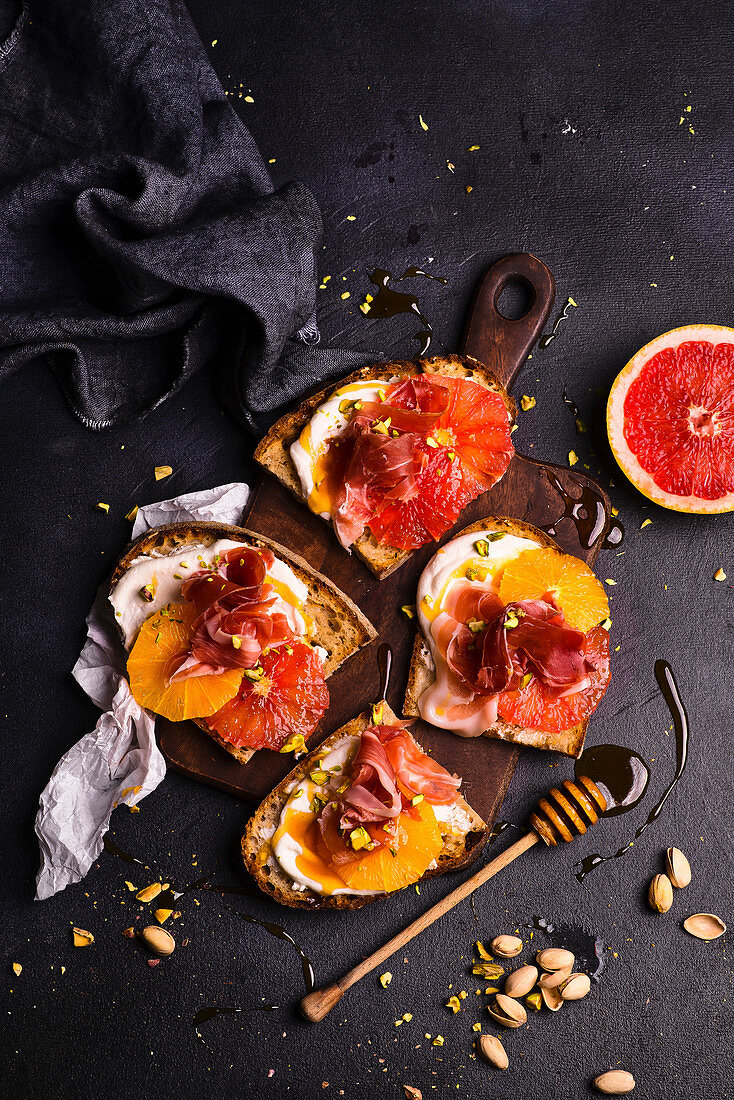 Toasts with creamy cheese, orange, grapefruit, Parma ham, honey and pistachios