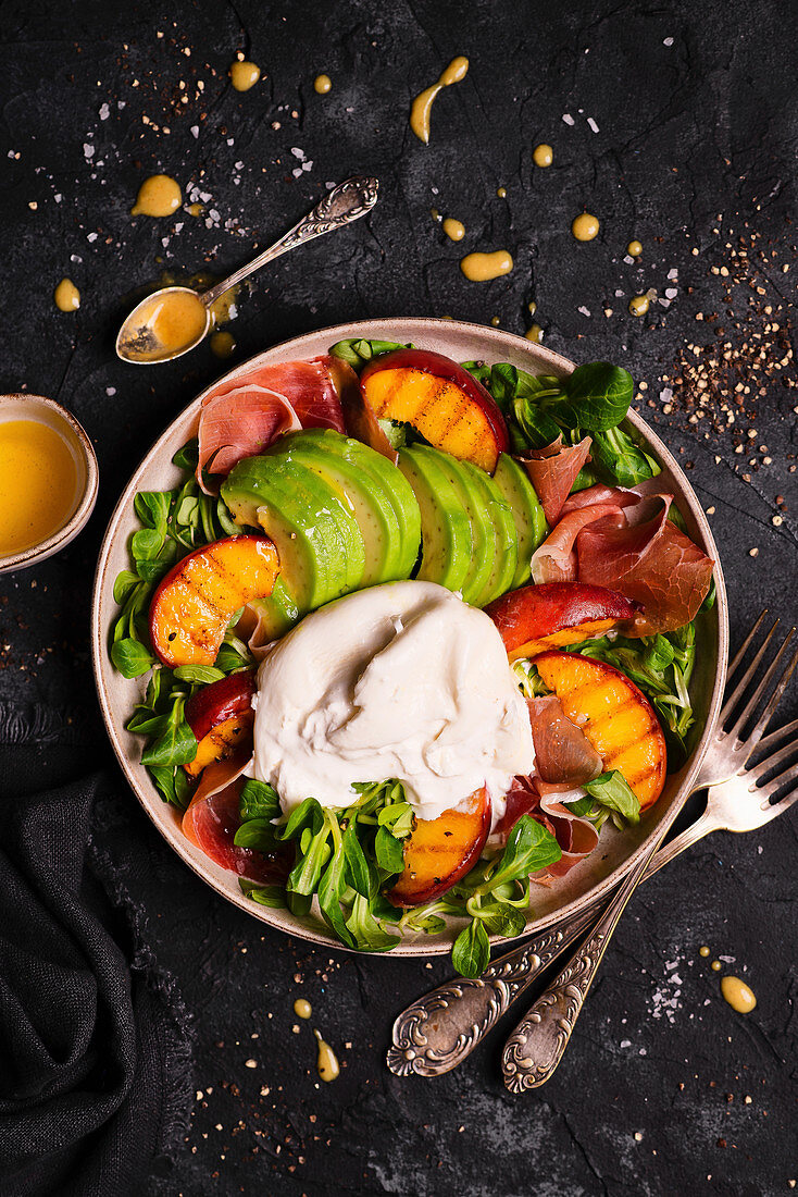 Salat mit Rucola, Pfirsichen, Avocado, Burrata und Parmaschinken