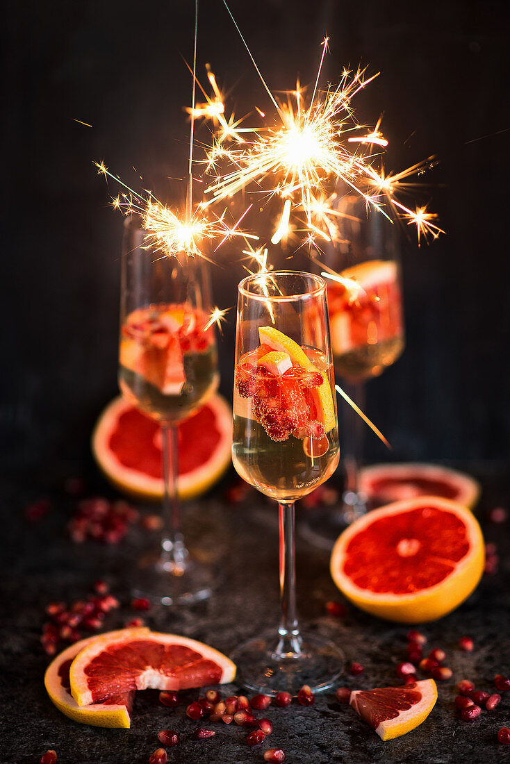 New Years Eve champagne in glasses with grapefruits, pomegranate seeds and sparklers