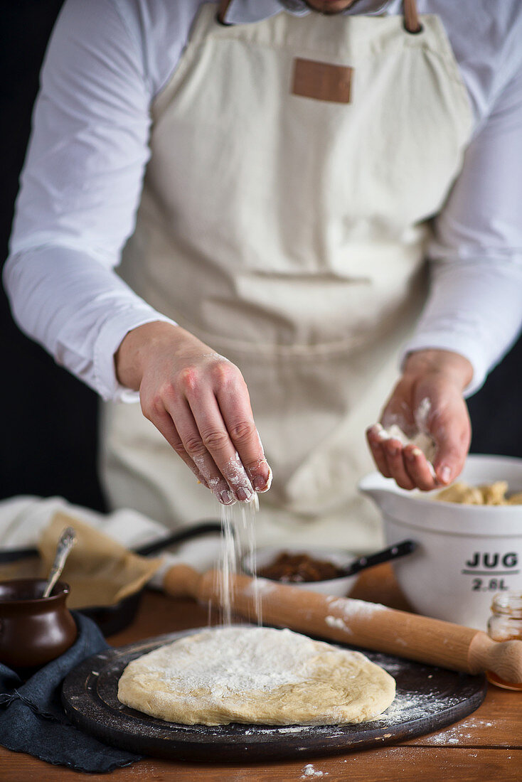Man baking in kitchen, sprinkling flour on yeast dough