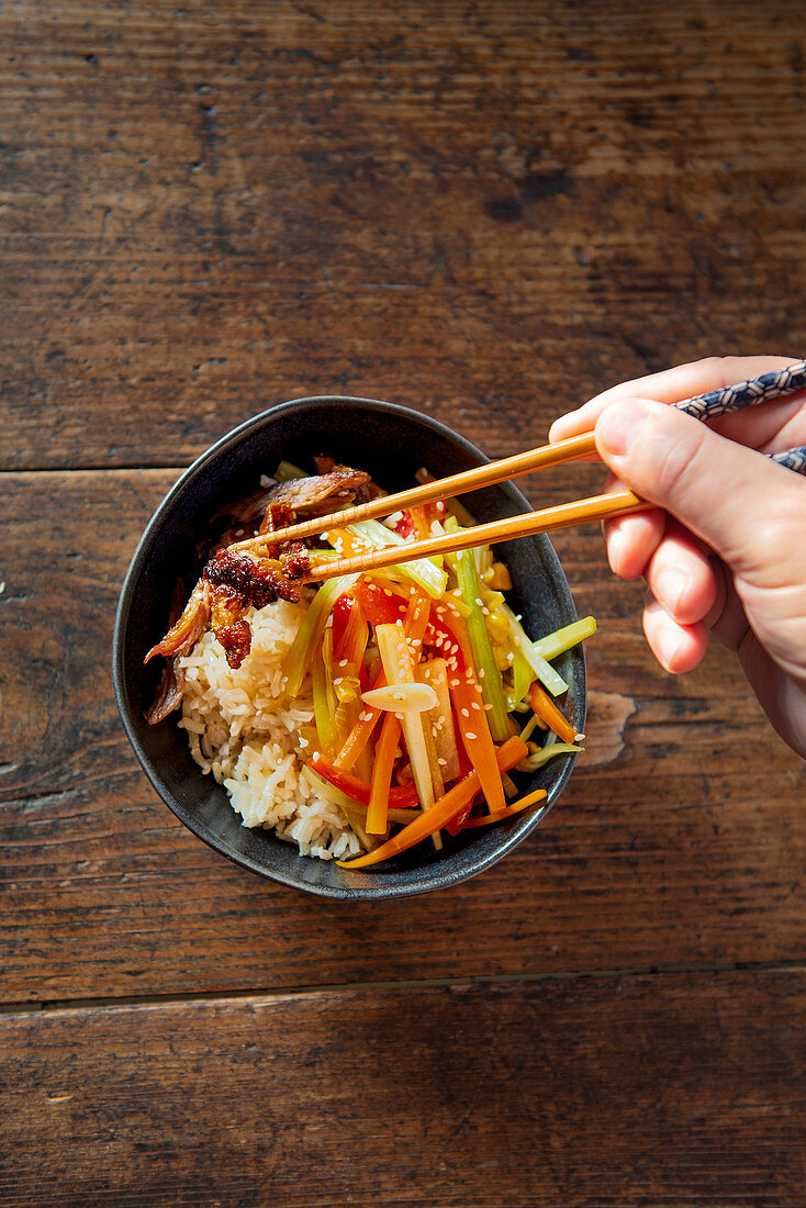 Hands taking Chinese vegetable and duck stir fry with chopsticks