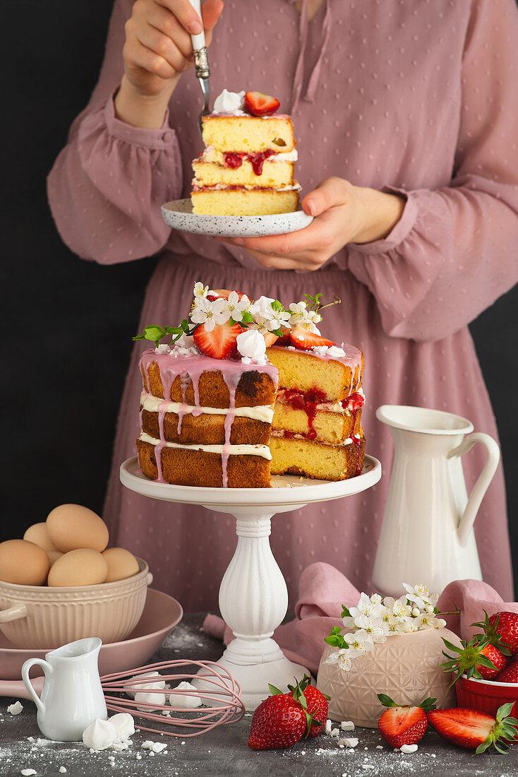 Frau isst ein Stück Biskuitkuchen mit Schlagsahne und Erdbeersauce