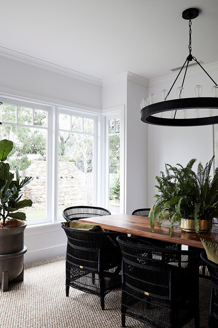 Dining table with black rattan armchairs, above it ring-shaped pendant lamp