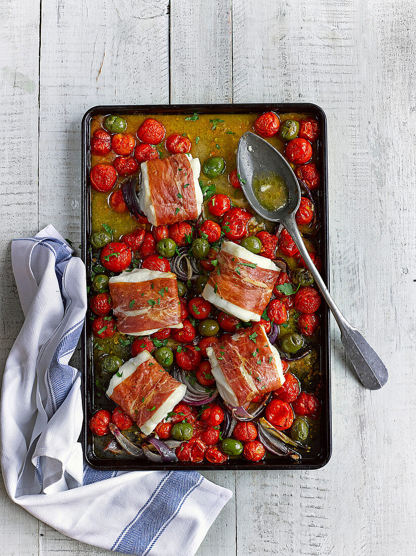 Baked cod wrapped in bacon with cherry tomatoes and olives