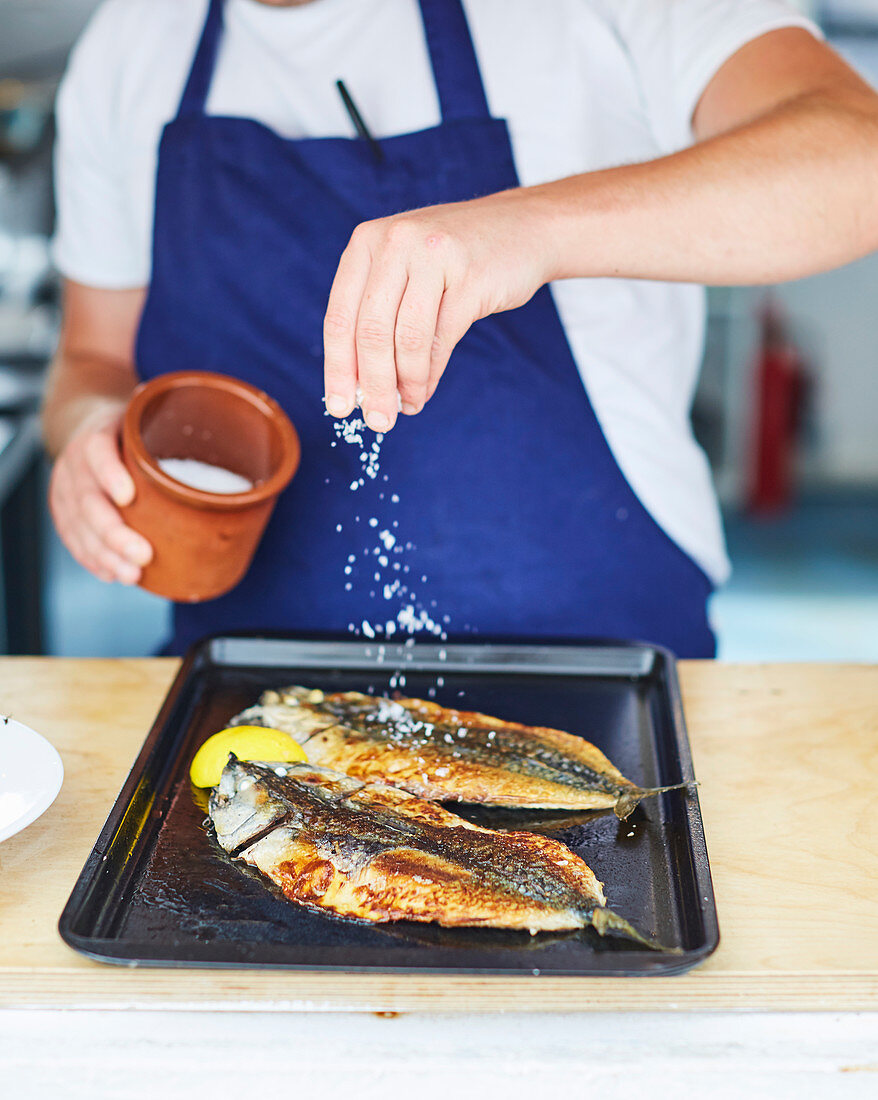 Sprinkling fried fish on a baking tray with sea salt
