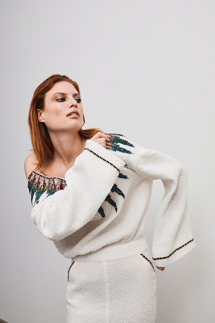 A red-haired woman wearing a white designer dress embroidered with rhinestones