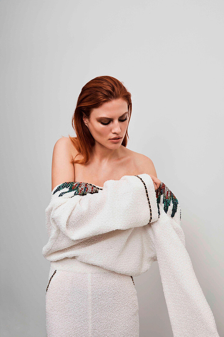 A red-haired woman wearing a white designer dress embroidered with rhinestones