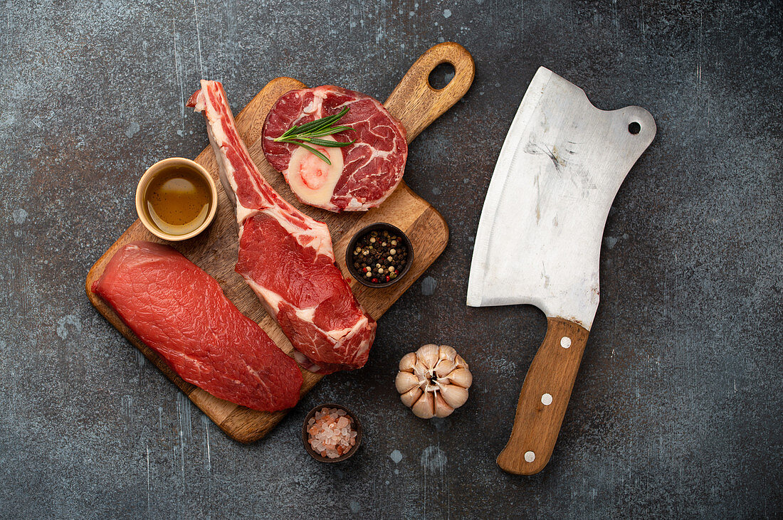 Assorted meat cuts and different steaks on wooden board, rustic meat cleaver