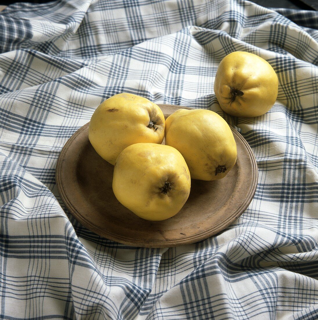 Three quinces on wooden plate, one beside it