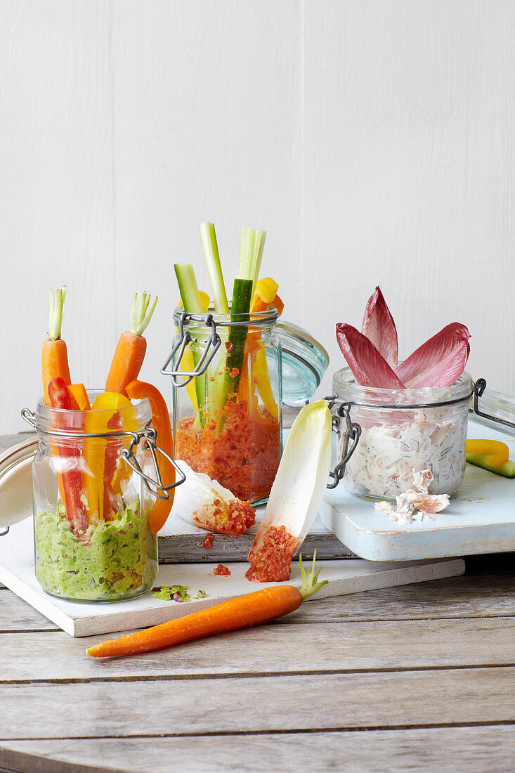Drei Picknick-Dips (Erbsen-Guacamole, Räucherlachs, gebratene Paprika) mit Gemüsesticks im Glas