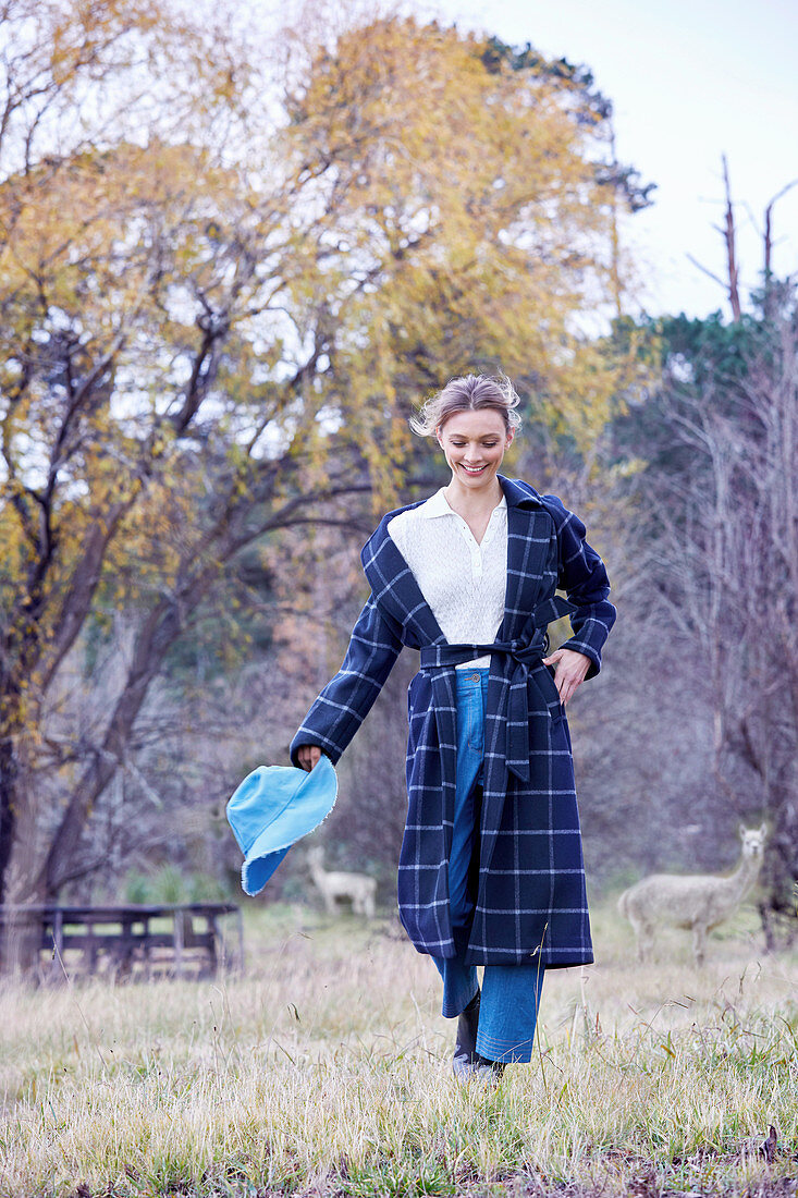 A blonde woman in a garden wearing a long, checked coat