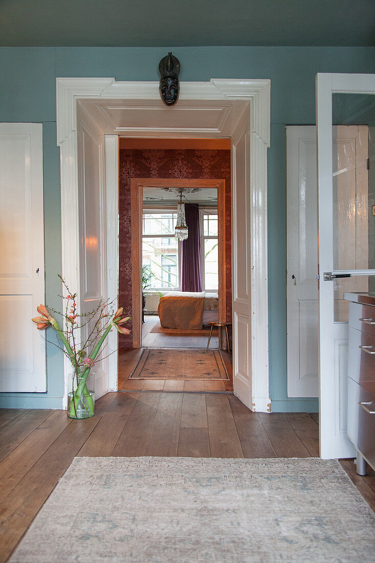 Floor vase of amaryllis next to white door frame in blue wall