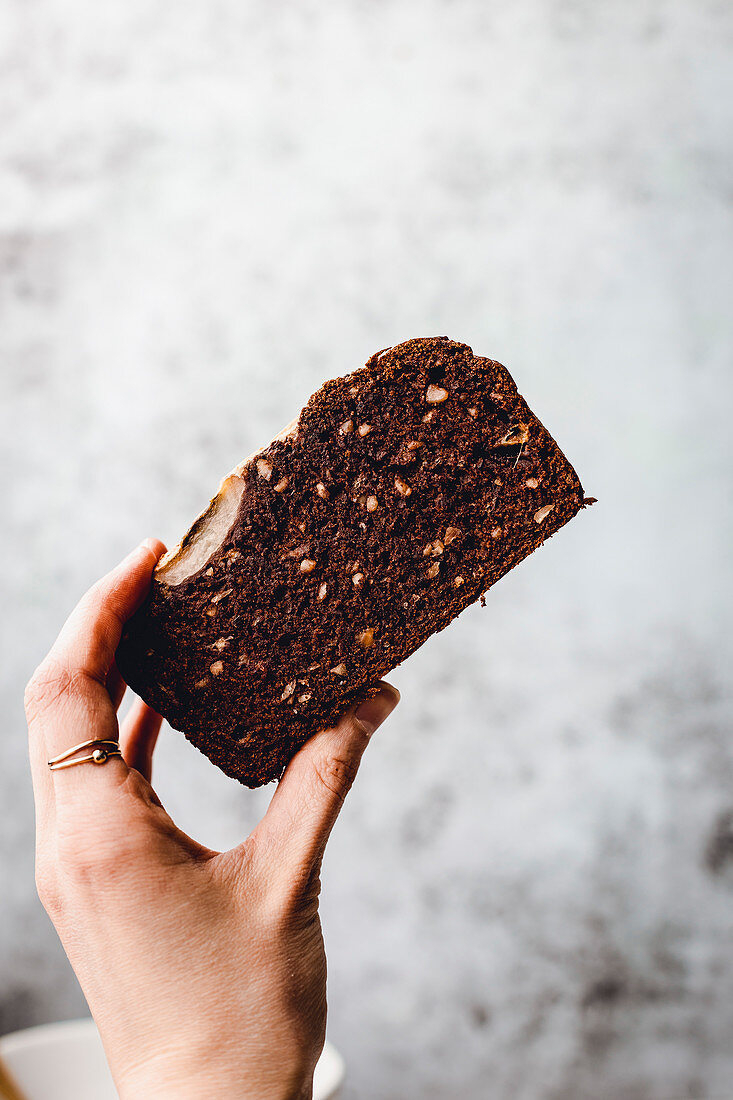 Hand hält eine Scheibe veganes Schokoladen-Bananenbrot