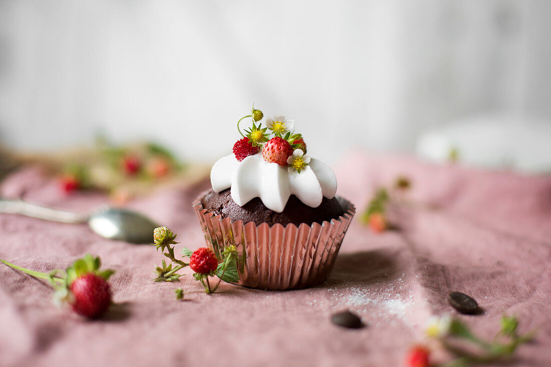 Chocolate cupcake with whipped cream and wild strawberries on the table