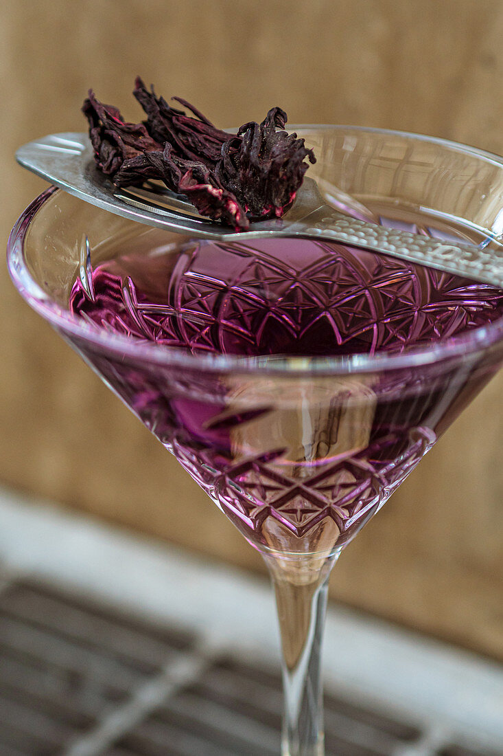 Metalllöffel mit getrockneten Blütenblättern auf Glas mit violettem Cocktail