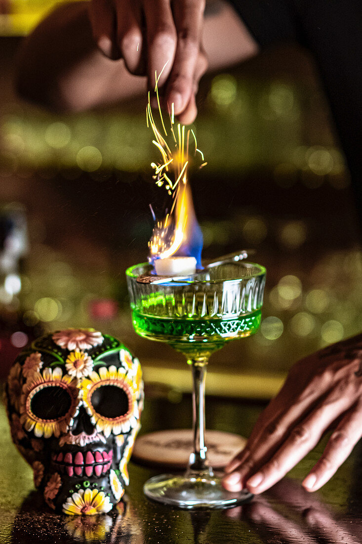 Unrecognizable crop barman standing at counter in bar and burning green alcohol drink