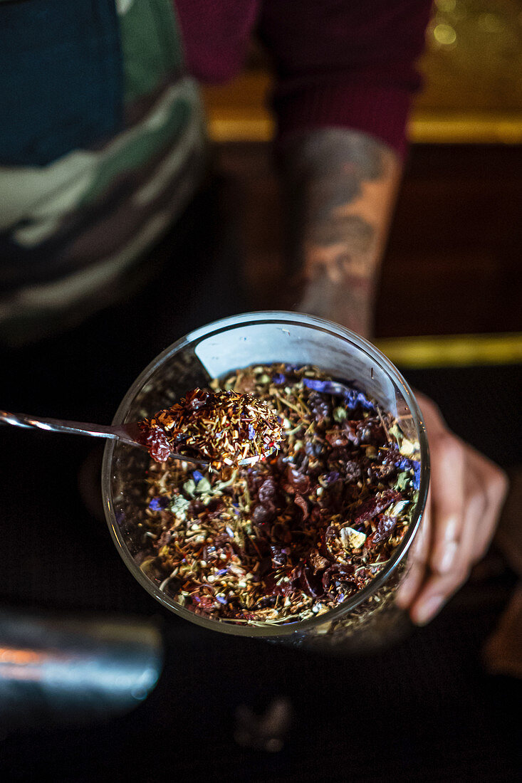 Anonymous man taking dried herbs from cup while preparing drink in bar