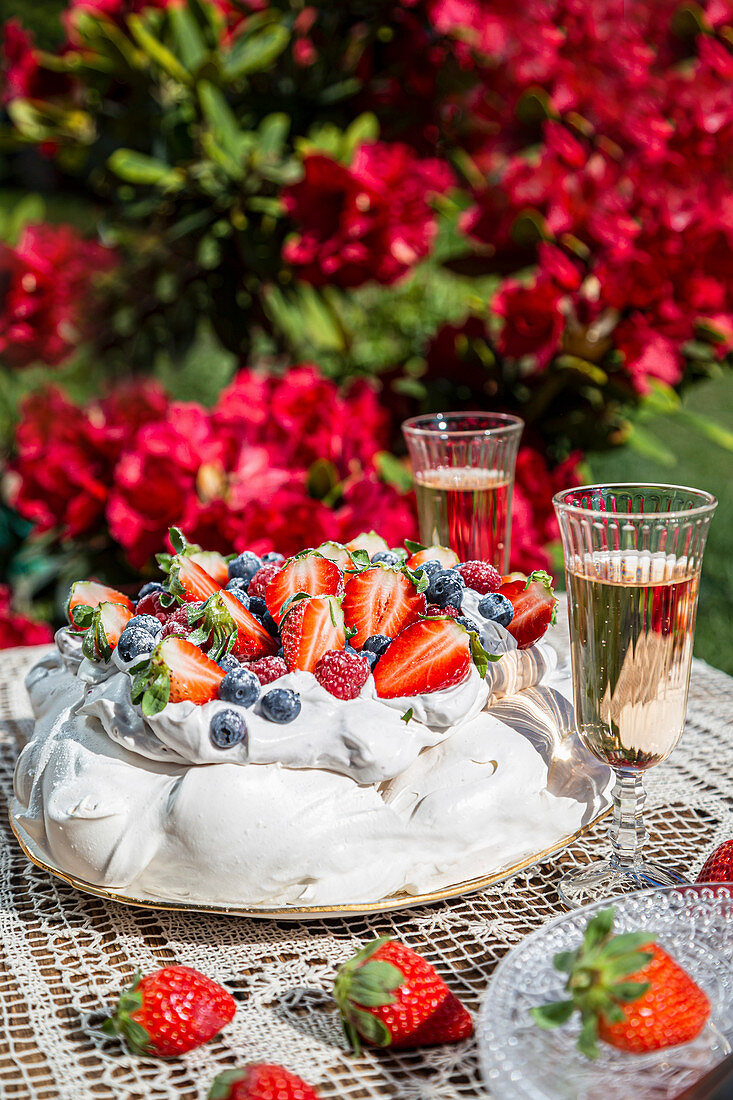 Pavlova with cream and fresh fruit served in the garden with champagne