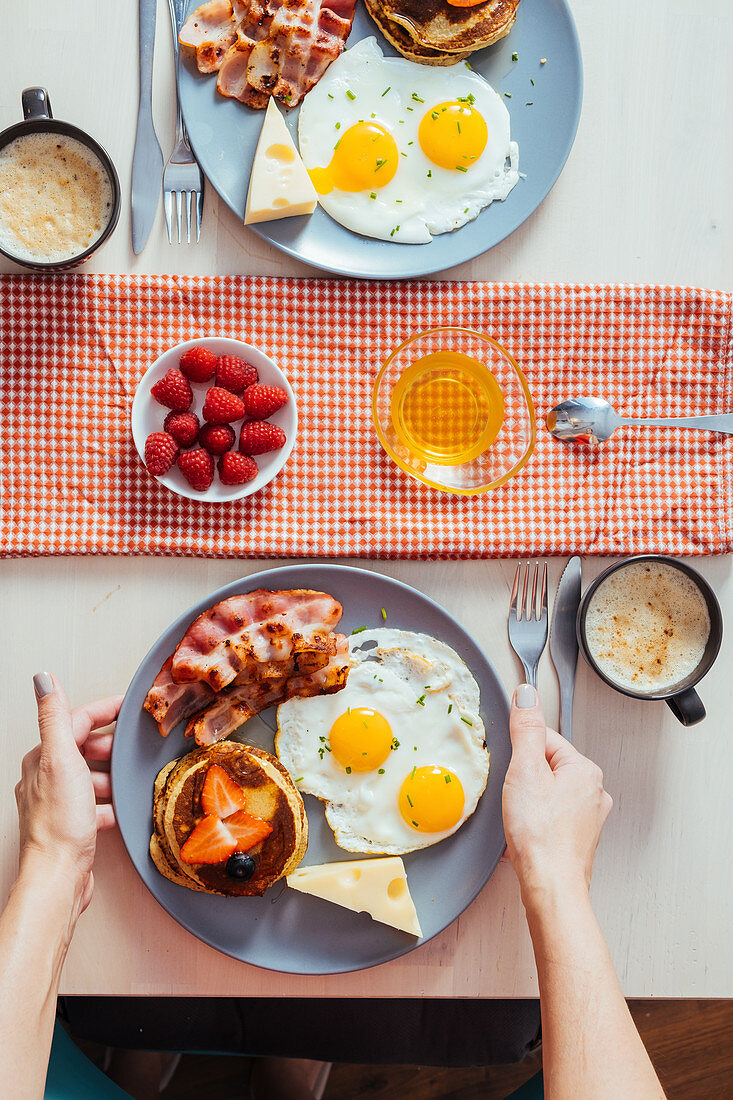 Frühstücksteller mit Pancakes, Spiegeleiern, Bacon und Käse