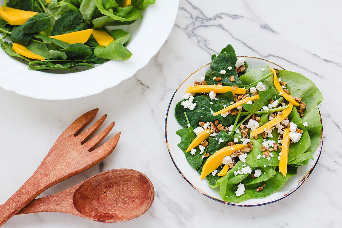 Bowl with healthy organic salad of green spinach topped with thin slices of pumpkin and goat cheese with walnuts