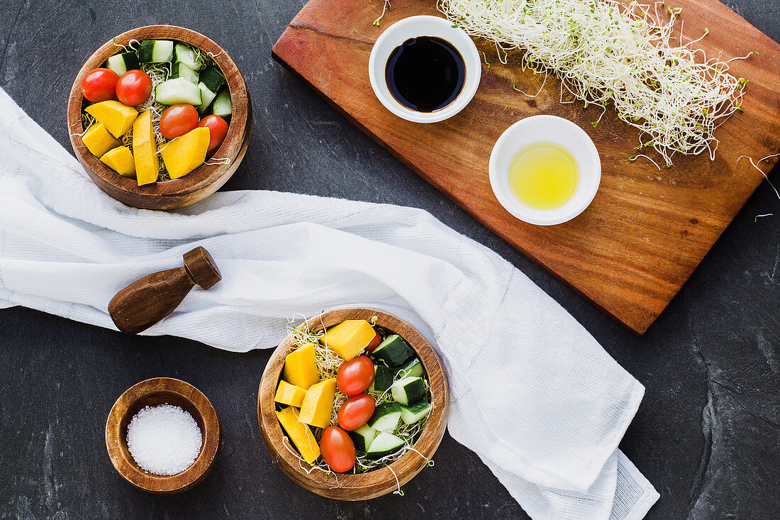 Wooden bowls filled with microgreens and topped with raw zucchini and pumpkins with cherry tomato on slate surface