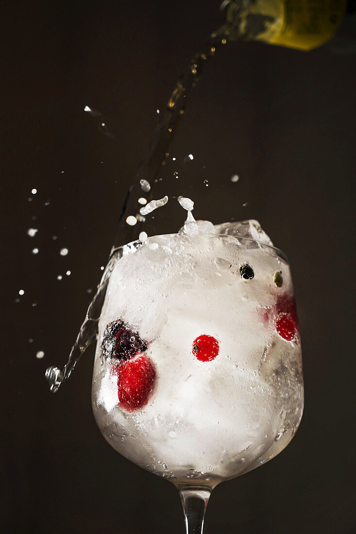 Refreshing transparent cocktail with sparkling water in glass of ice and berries on dark background