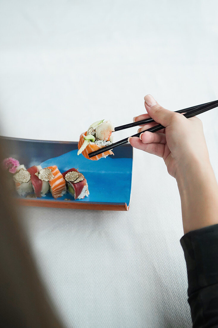 Holding sushi with chopsticks above white wooden table