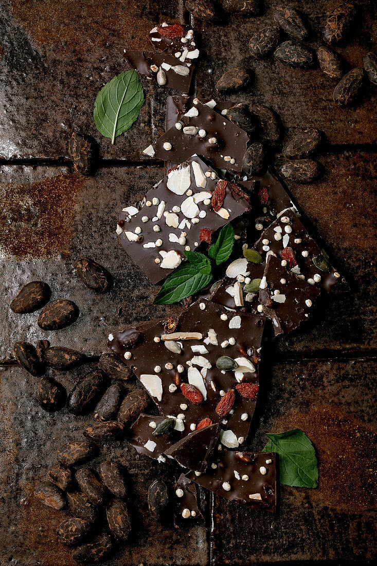 Handmade chopped dark chocolate with different superfood additives seeds and goji berries, cocoa beans and fresh mint