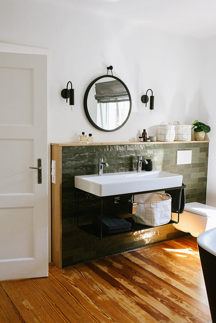 Sink with two sets of taps against green wall tiles with wooden frame