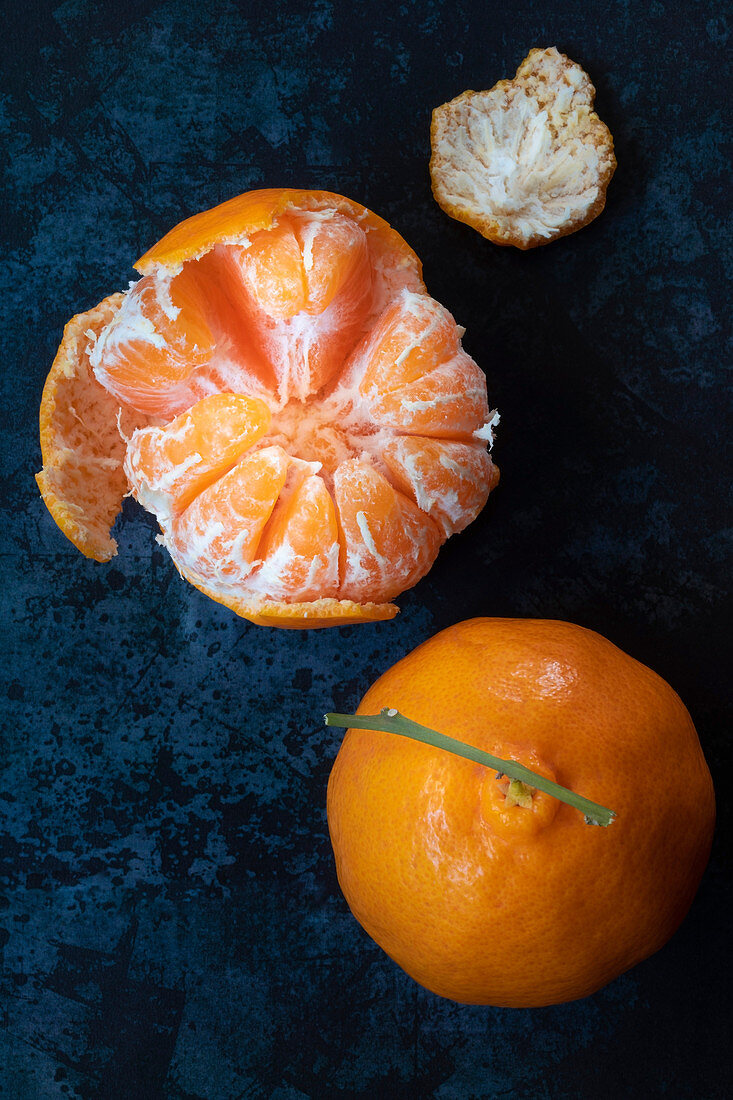 A peeled and whole mandarin on a blue background