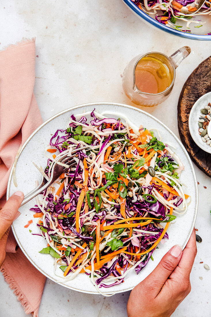 Lady holding a bowl of colorful vegan coleslaw, served with dressing