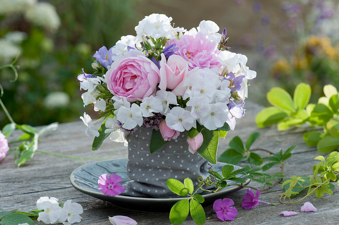 Kleiner Duftstrauß aus Flammenblumen, Rosen, Glockenblumen und Salbeiblättern in Stoffsäckchen auf Teller gestellt