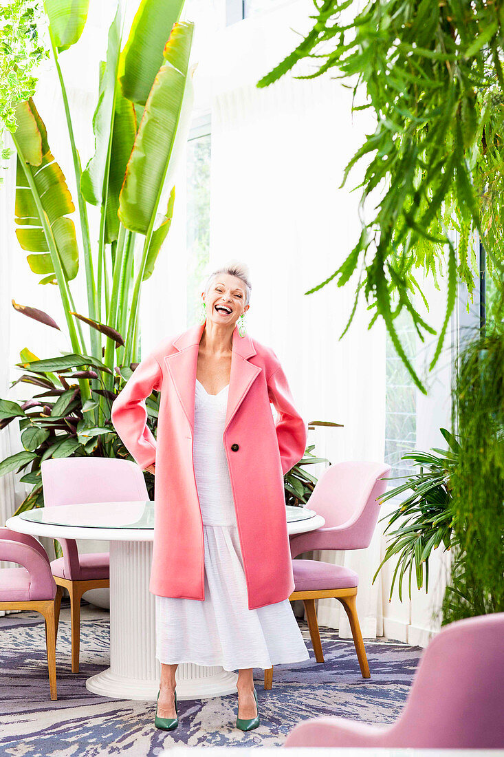 A grey-haired woman wearing a pink coat over a long white skirt