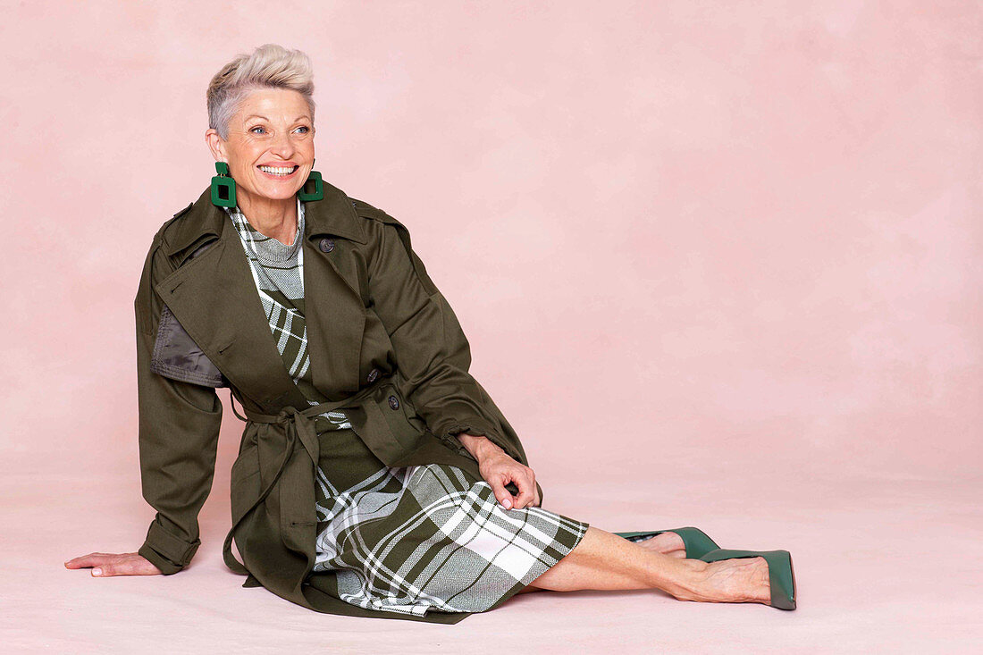 A grey-haired woman wearing a green checked dress and a green coat