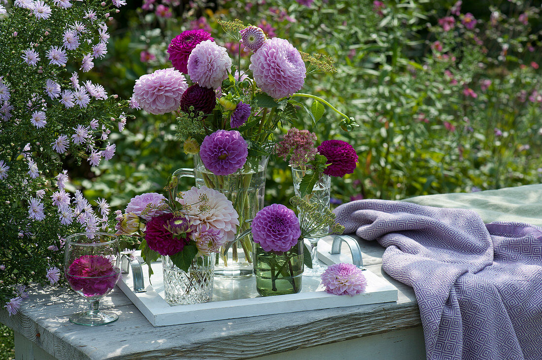 Small bouquets with dahlias, fennel umbels, cartilage carrots and sedum plants in glasses on a wooden tray