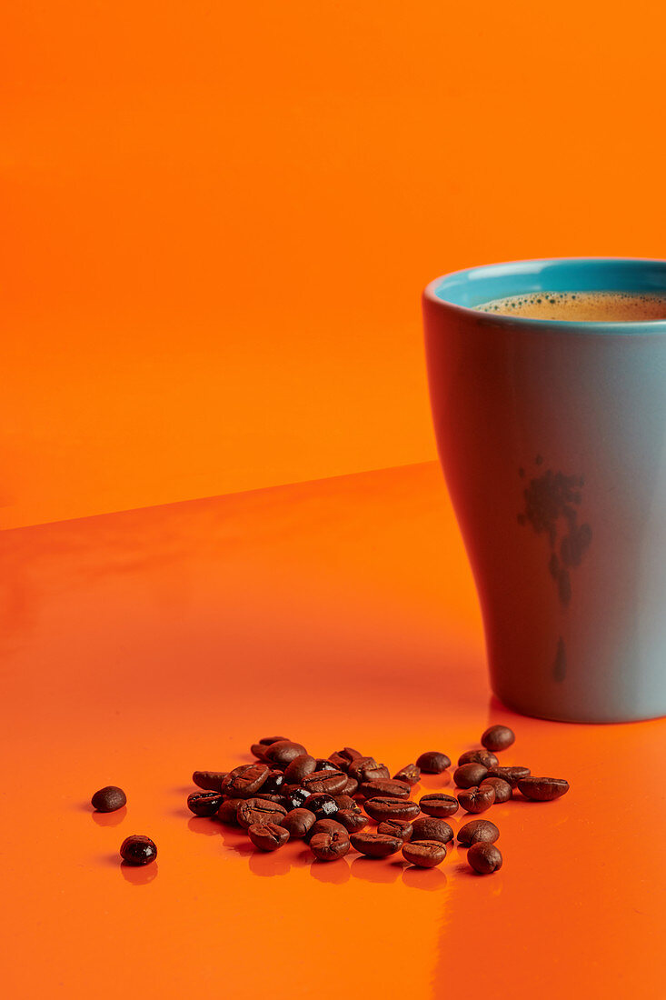 Becher heißer Kaffee und Kaffeebohnen auf orangefarbenem Untergrund