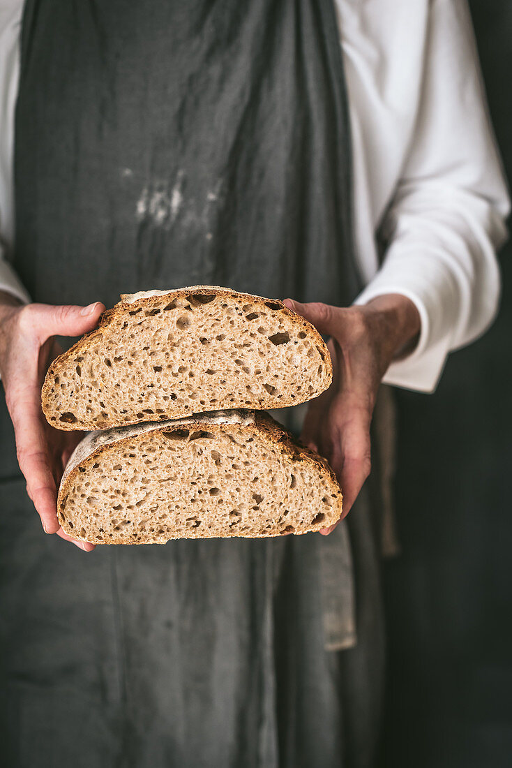Cropped unrecognizable baker in apron with loaf of tasty bread cut in half placed
