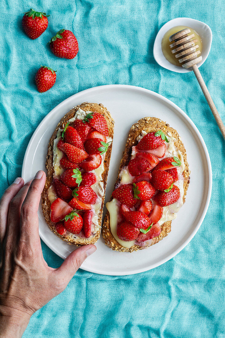 Hand greift nach Toastbrot mit frischen Erdbeeren und Honig