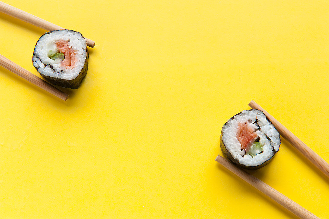 Rolls with rice and salmon placed on colorful yellow table with chopsticks in studio