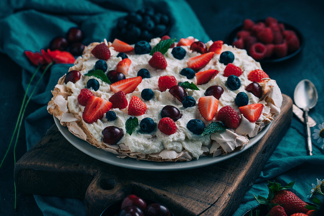 Delectable sweet meringue Pavlova cake with assorted fresh berries including strawberry and raspberry with cherry and blueberry