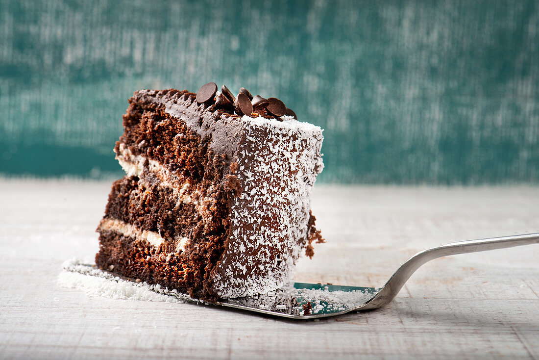 Chocolate cake slice with cream and coconut placed against shabby background