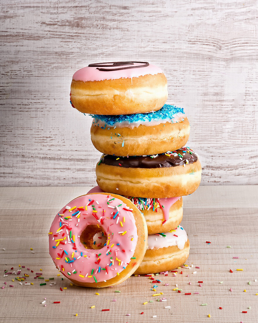 Stack of yummy sweet assorted donuts with colorful frosting and sprinkles placed on wooden background