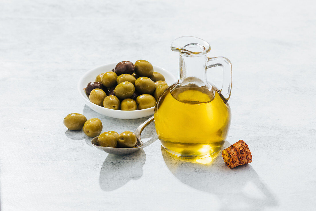 Olivenöl im Glaskrug neben grünen Oliven